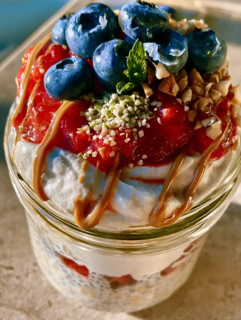 Sweet breakfast recipes: High-Protein Berry Cheesecake Overnight Oats 1 Top view of almond butter drizzle, hemp hearts, and toasted almonds on high-protein oats.