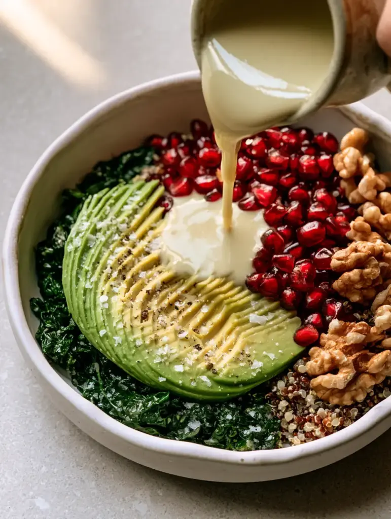 Silky lemon-tahini dressing being poured over a kale and quinoa bowl in a matte white ceramic bowl.