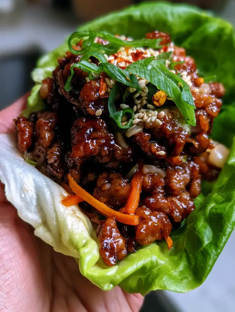 Detail shot of ground pork crumbles with minced water chestnuts, sesame seeds, and scallions in a lettuce cup.