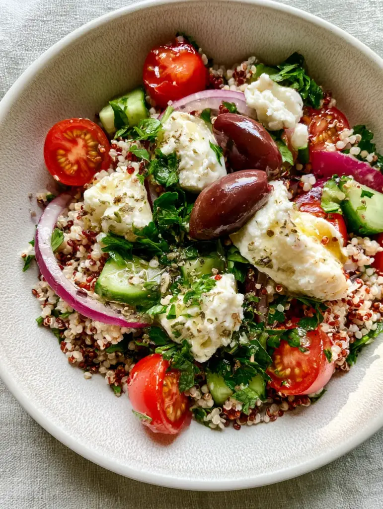 Close up shot of glossy kalamata olives and large crumbles of feta cheese atop a colorful quinoa salad.