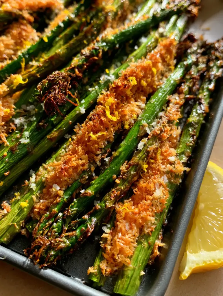 Close-up of crispy asparagus spears with toasted garlic bits, sea salt flakes, and a fresh lemon wedge.