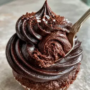 Close up photo of ebony-brown chocolate frosting recipes showing a silky sheen and dense airless interior texture.