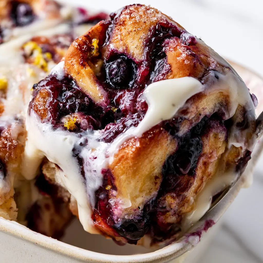 Extreme macro shot of bubbling sugar crust and fresh lemon zest on a blueberry cinnamon roll casserole.