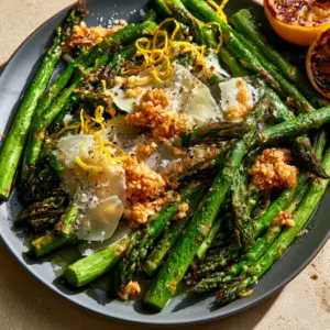 Top-down view of vibrant green oven roasted asparagus with garlic clusters and lemon zest. (oven roasted asparagus)