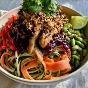 Close up of spiralized zucchini and ribboned carrots in a white ceramic bowl with water droplets (raw food recipes for beginners)